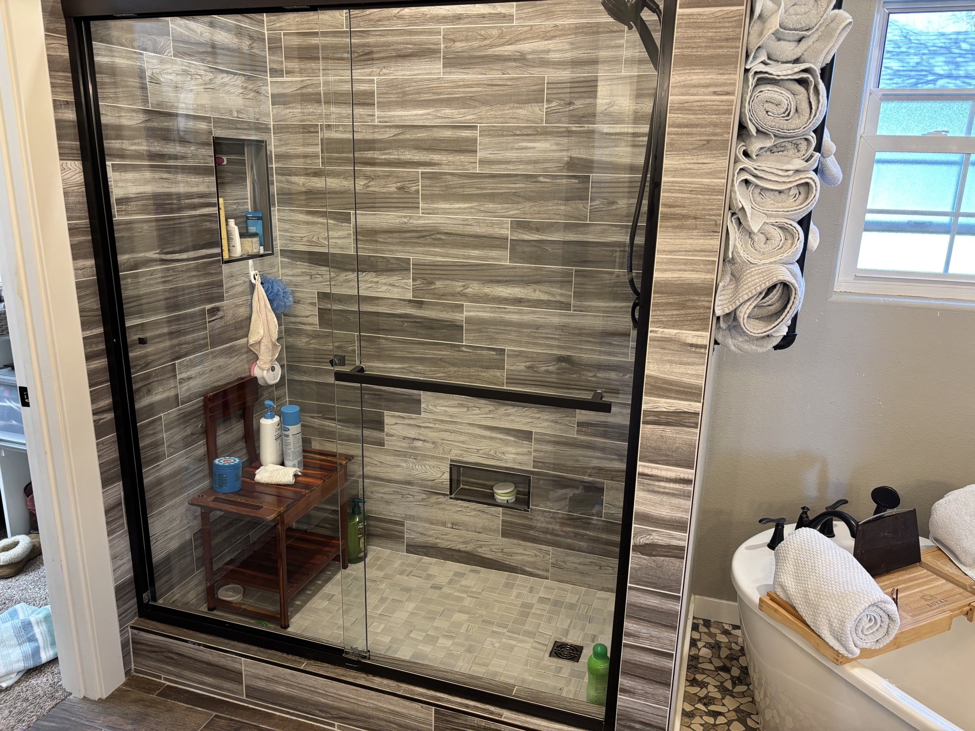A spotless MCCT-cleaned bathroom in Springfield with brown wood-look tile, glass shower, and rolled towels