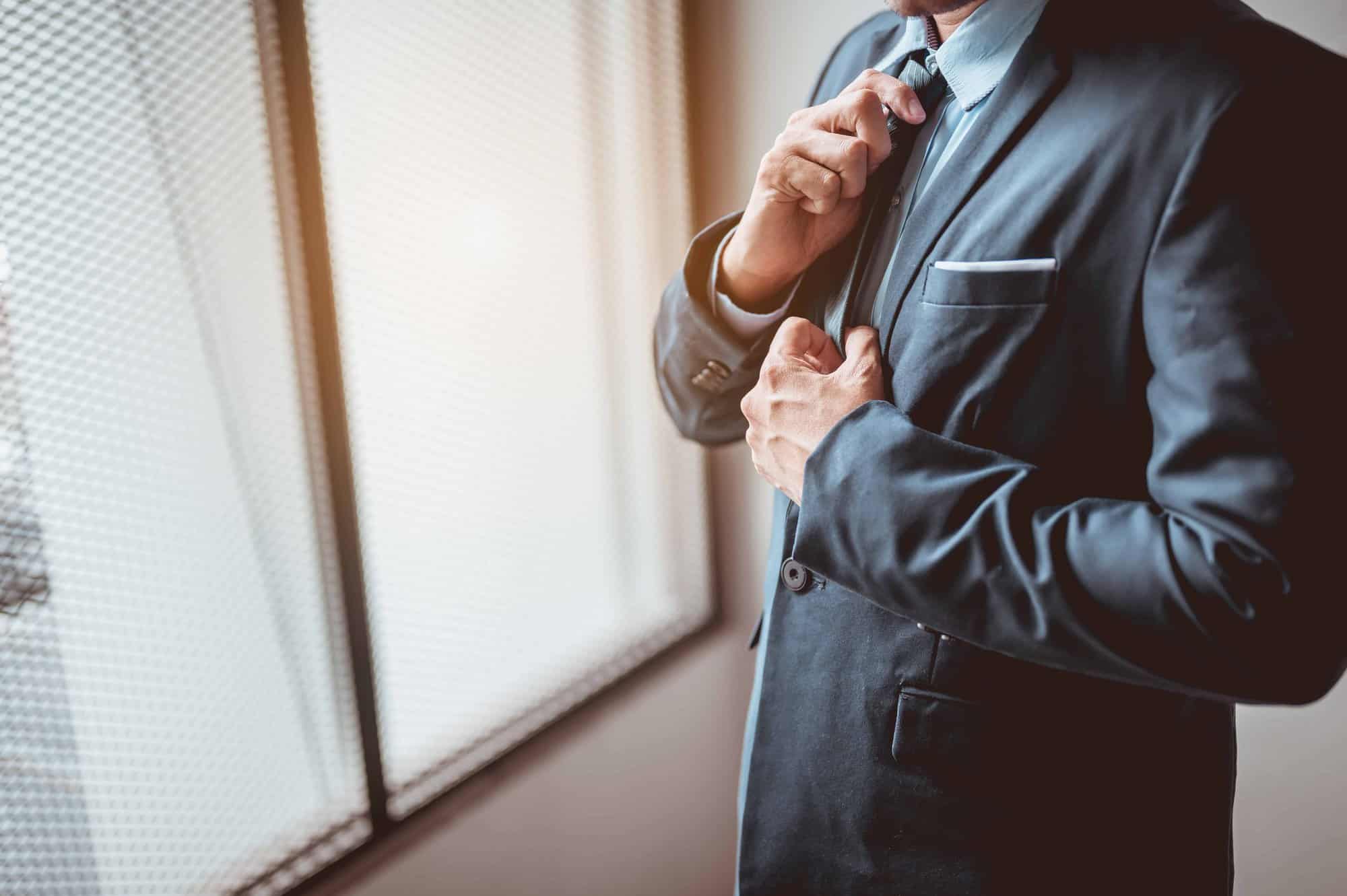 man adjusting tie looking out window
