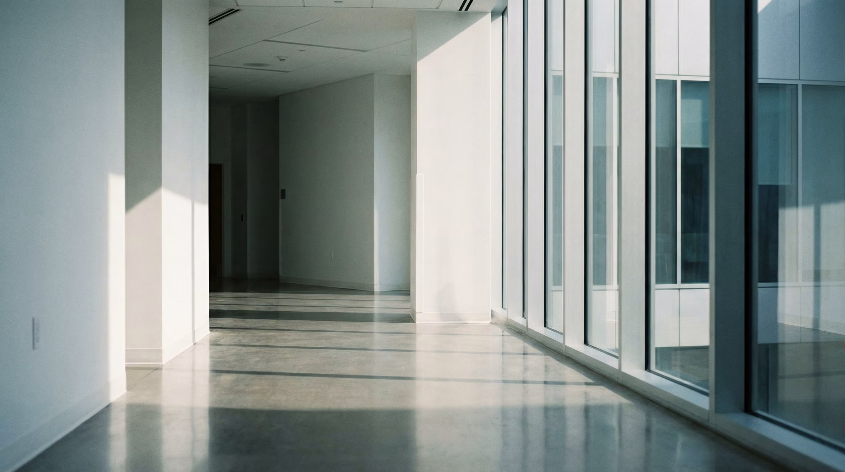 Empty bright corridor with polished concrete floors and floor-to-ceiling glass walls.
