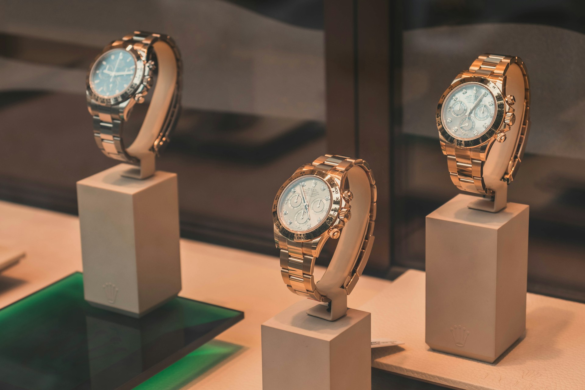 Three rose-gold chronograph watches displayed on white pedestals in a jewelry store case.