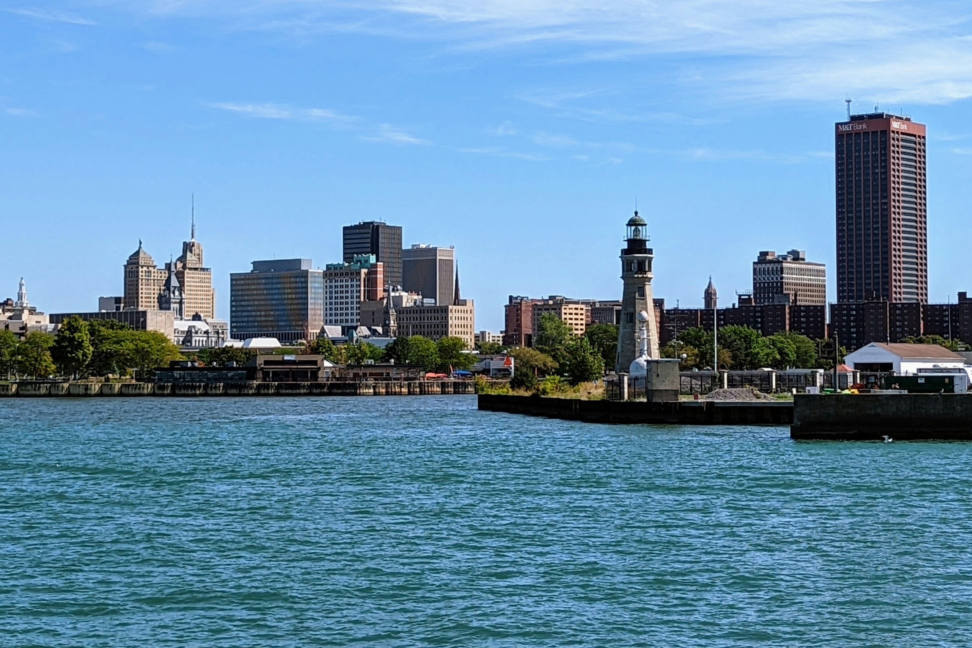 City skyline viewed across blue water with a waterfront lighthouse on a sunny day.
