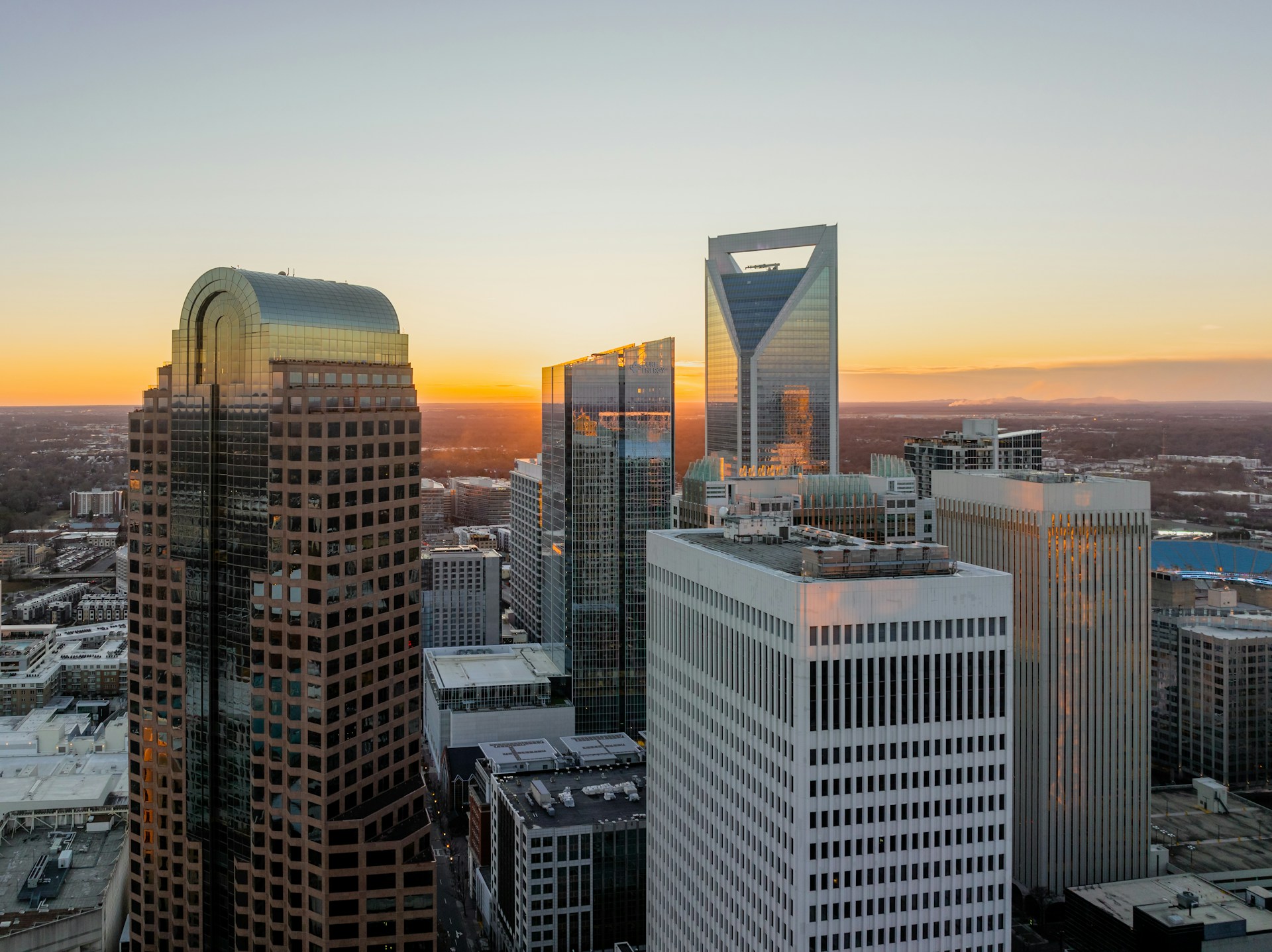 Glass and steel downtown towers glowing amber against an orange sunset sky.