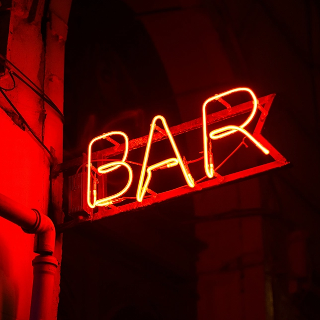 Red neon sign glowing with the word BAR on a dark building exterior at night.