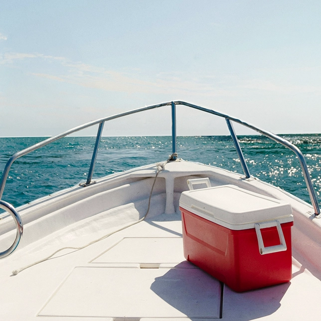 View of a boat bow with a red cooler on deck, looking out at the sparkling ocean under a clear sky.