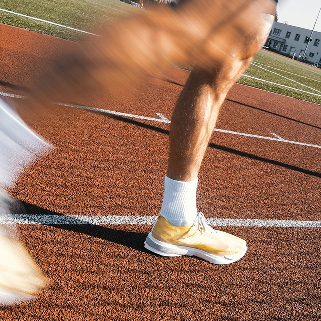 Runner's legs in motion on a red track, wearing white socks and yellow running shoes.