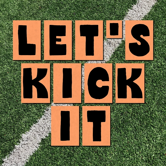 Orange cards with black letters spelling LET'S KICK IT on green turf with a white line.