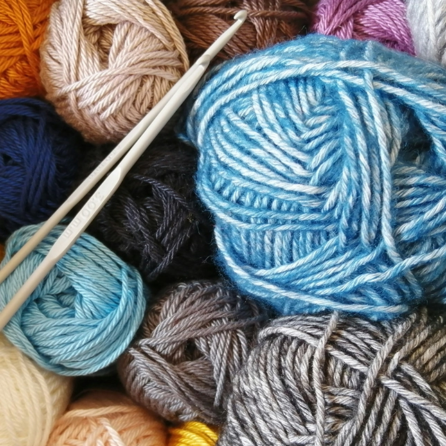 Multiple balls of yarn in various colors with two white crochet hooks resting on them.
