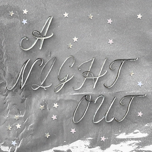 Script text reading 'A NIGHT OUT' on a gray crumpled surface with small pastel star confetti around.