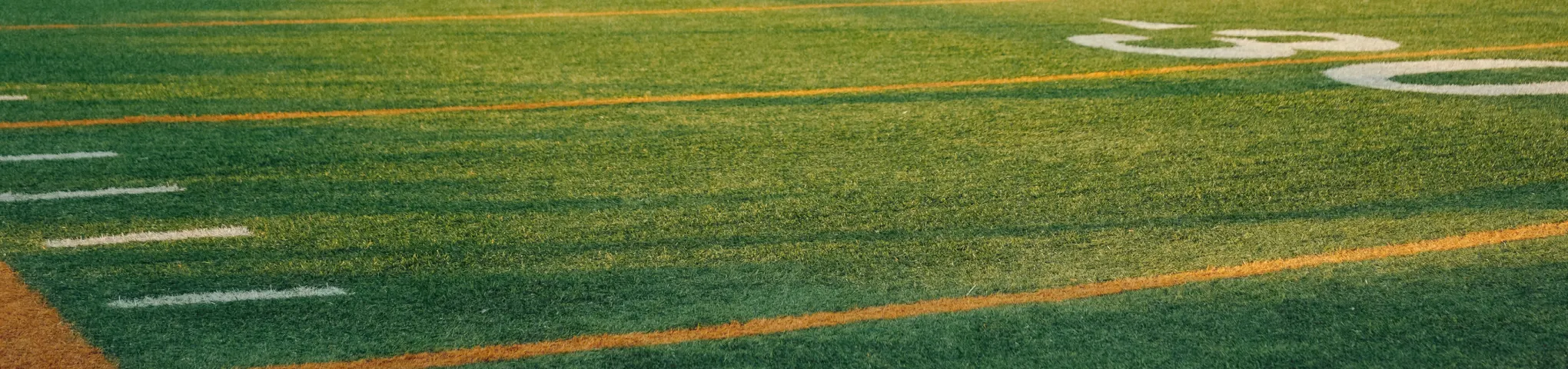 Close-up of a green sports field with yellow and white yard lines and numbers.