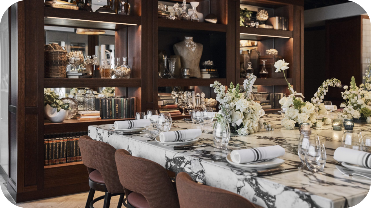 Elegant dining area with marble table, floral centrepieces, and rich timber shelving styled with books and décor.