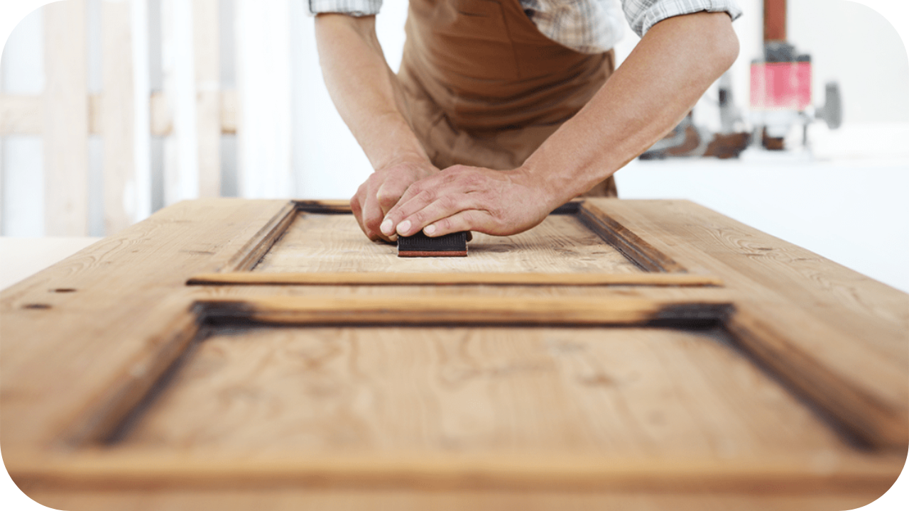 Carpenter sanding a wooden door panel to achieve a smooth finish during joinery work.