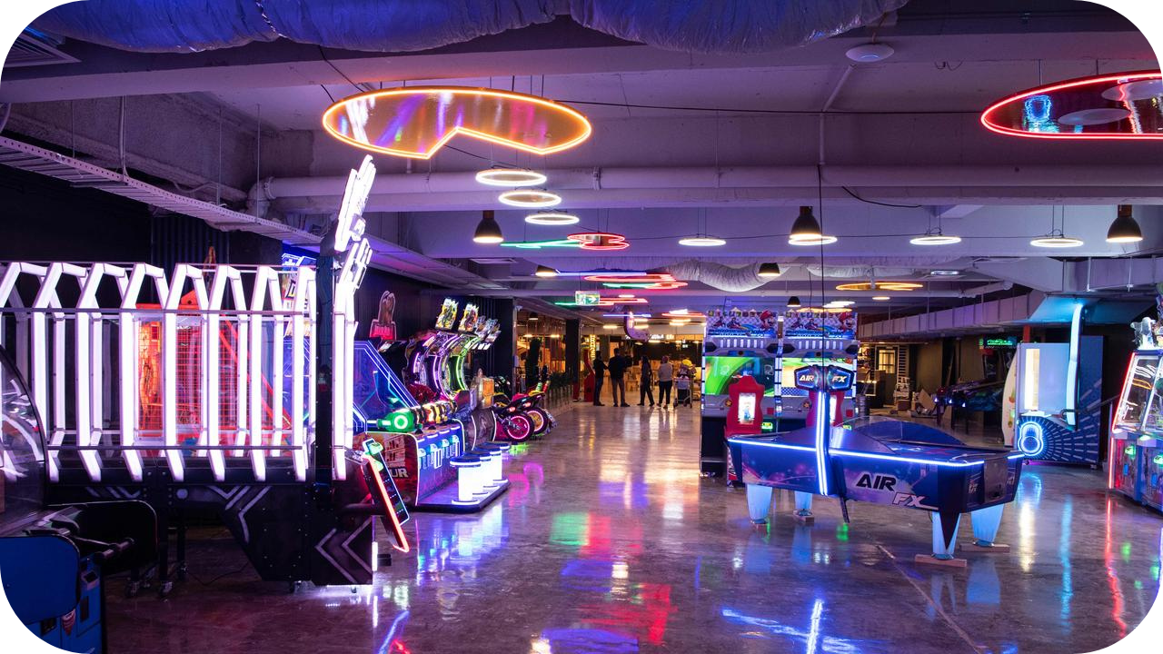 Neon-lit arcade space with gaming machines, air hockey table, and colourful ceiling lights.