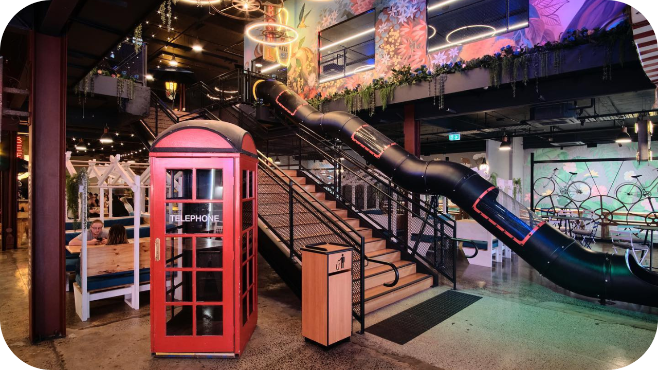 Creative office fit-out featuring a red phone booth, staircase with black slide, and vibrant wall murals.