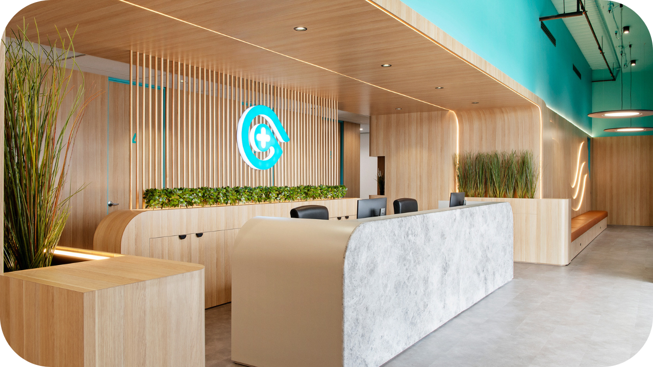 Contemporary healthcare reception with timber slat detailing, stone-front desk, indoor greenery, and branded signage.