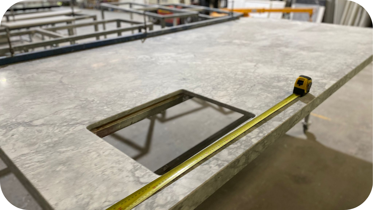 Measuring a marble benchtop cut-out with a tape measure in a joinery workshop, ensuring precise fit for kitchen installation.