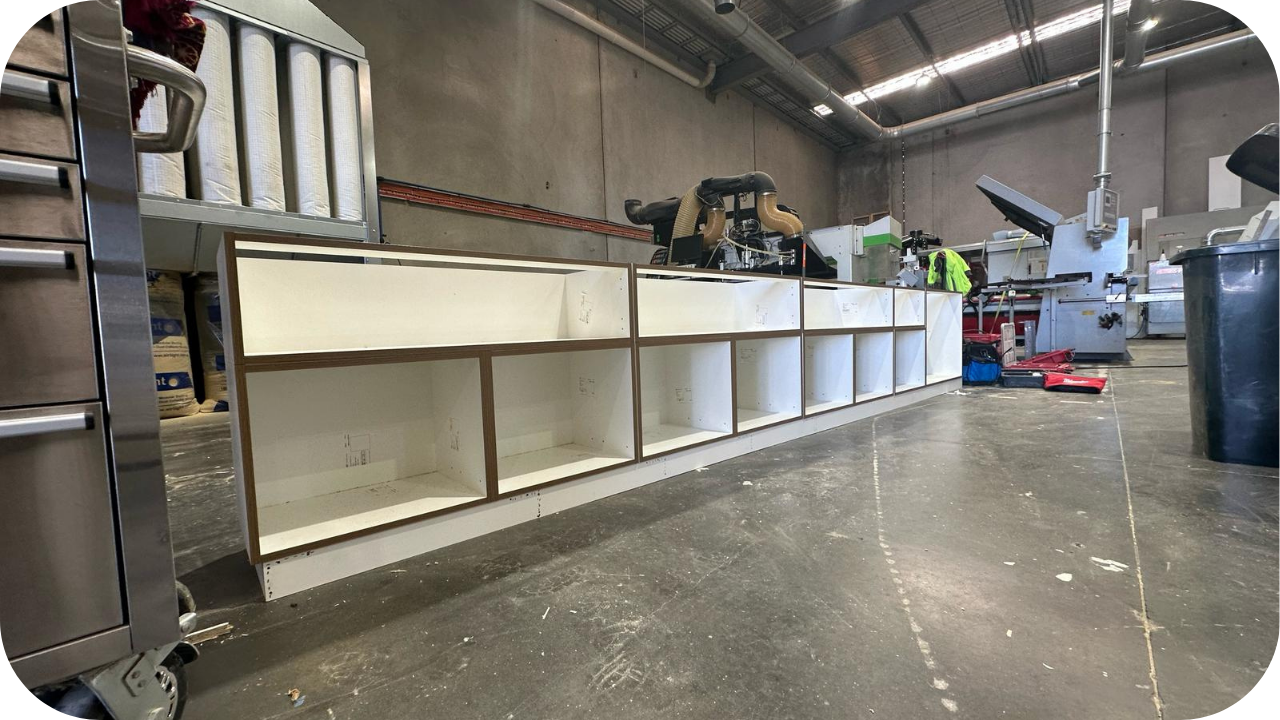 Long kitchen cabinet frame under construction in a joinery workshop, showing open compartments and precise craftsmanship in progress.