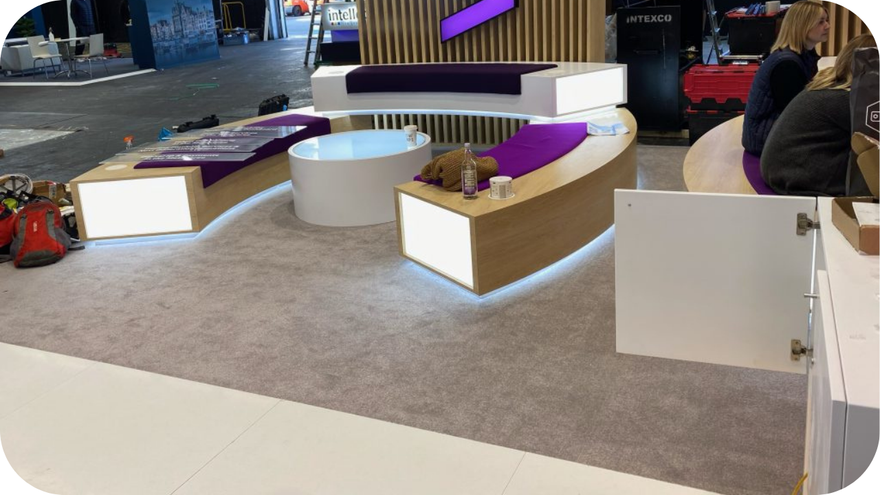 A partially assembled exhibition stand with curved seating, built-in lighting, and custom joinery elements illustrating key practical considerations for event setups.