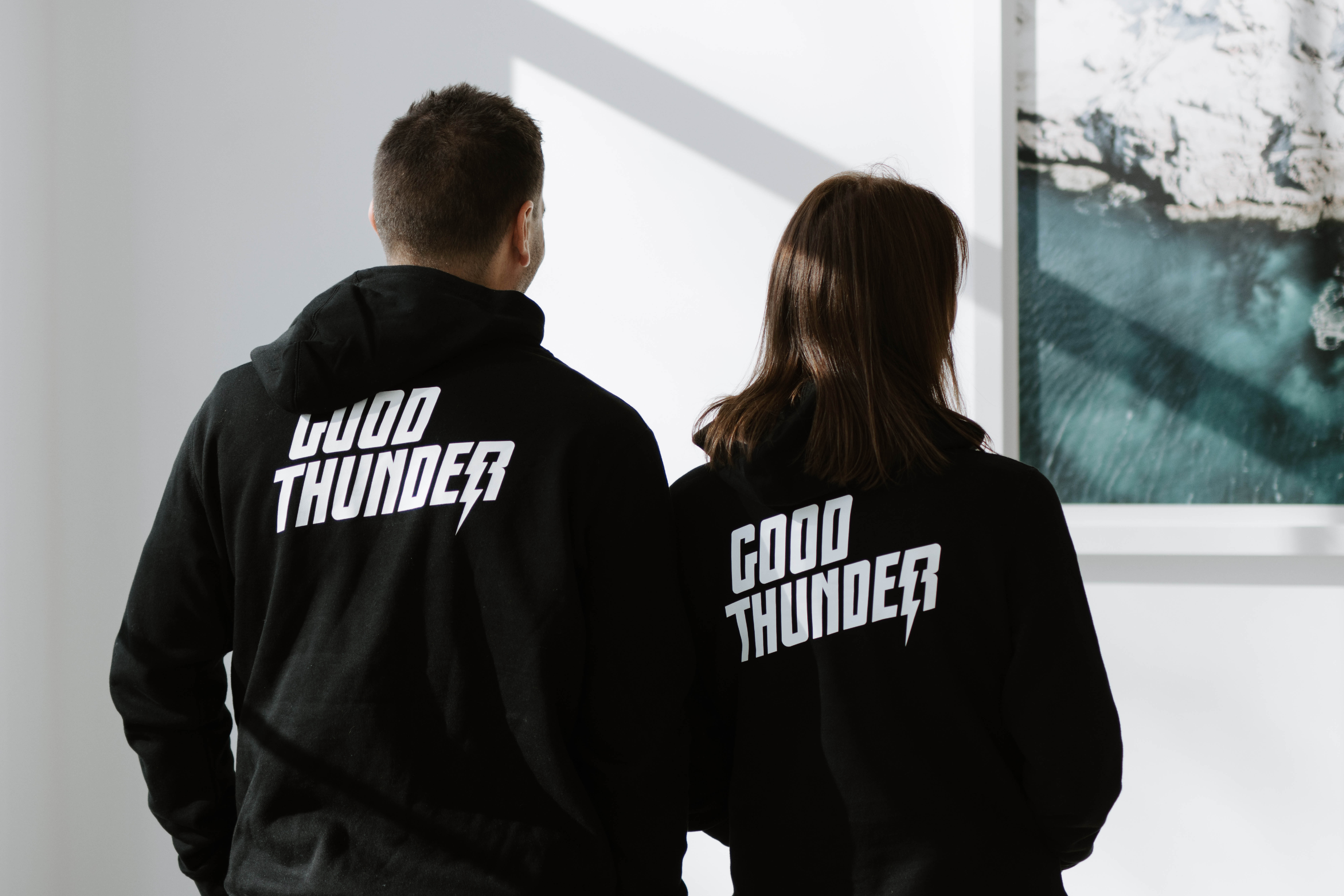 Two people wearing black hoodies with 'GOOD THUNDER' and a lightning bolt graphic on the back.