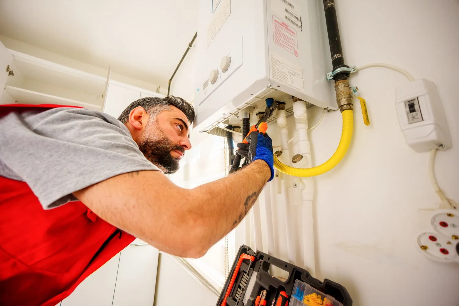 A technician uses a wrench to adjust plumbing or connections on a wall-mounted boiler.