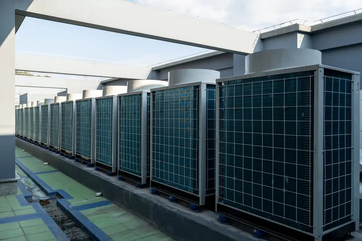 A long row of central air conditioning units sits on a flat commercial rooftop.