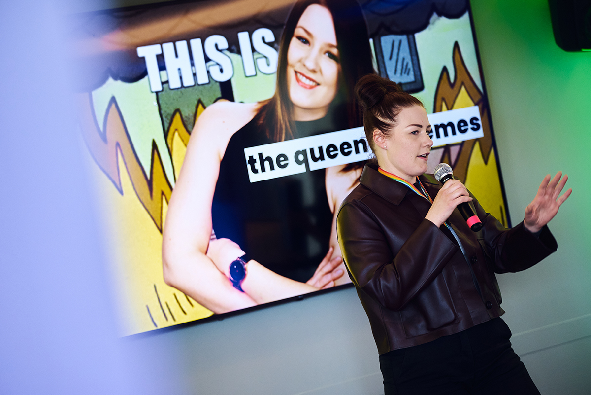 Anni Salo speaking into a microphone in front of the queen of memes slide