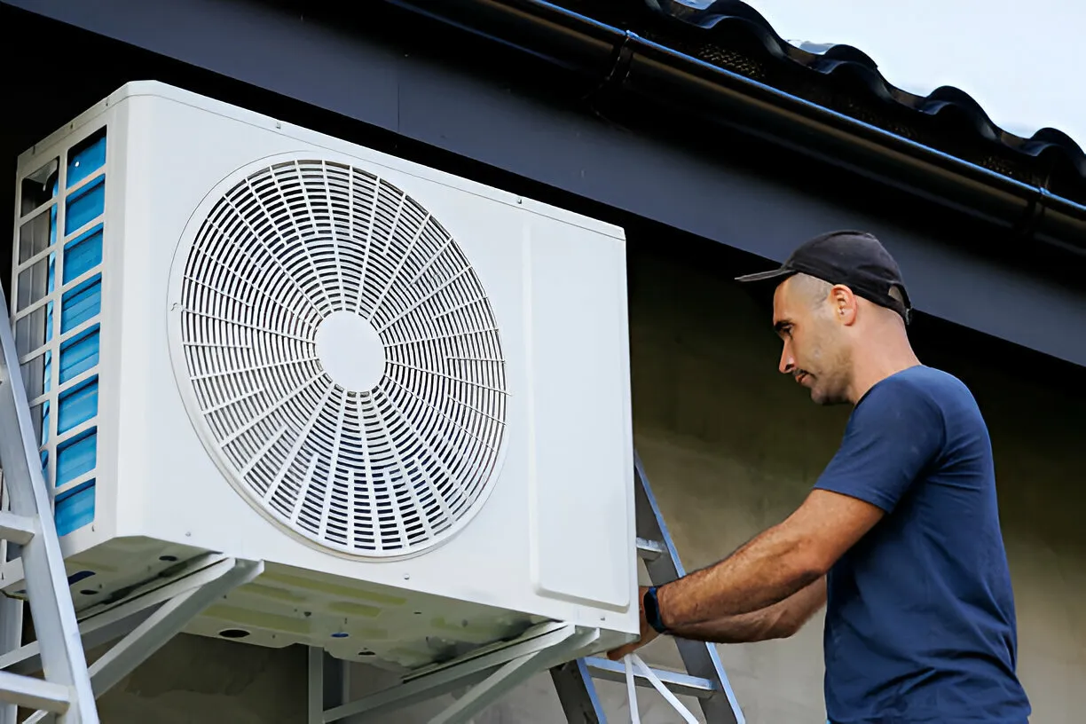 Man on ladder repairing outdoor AC.