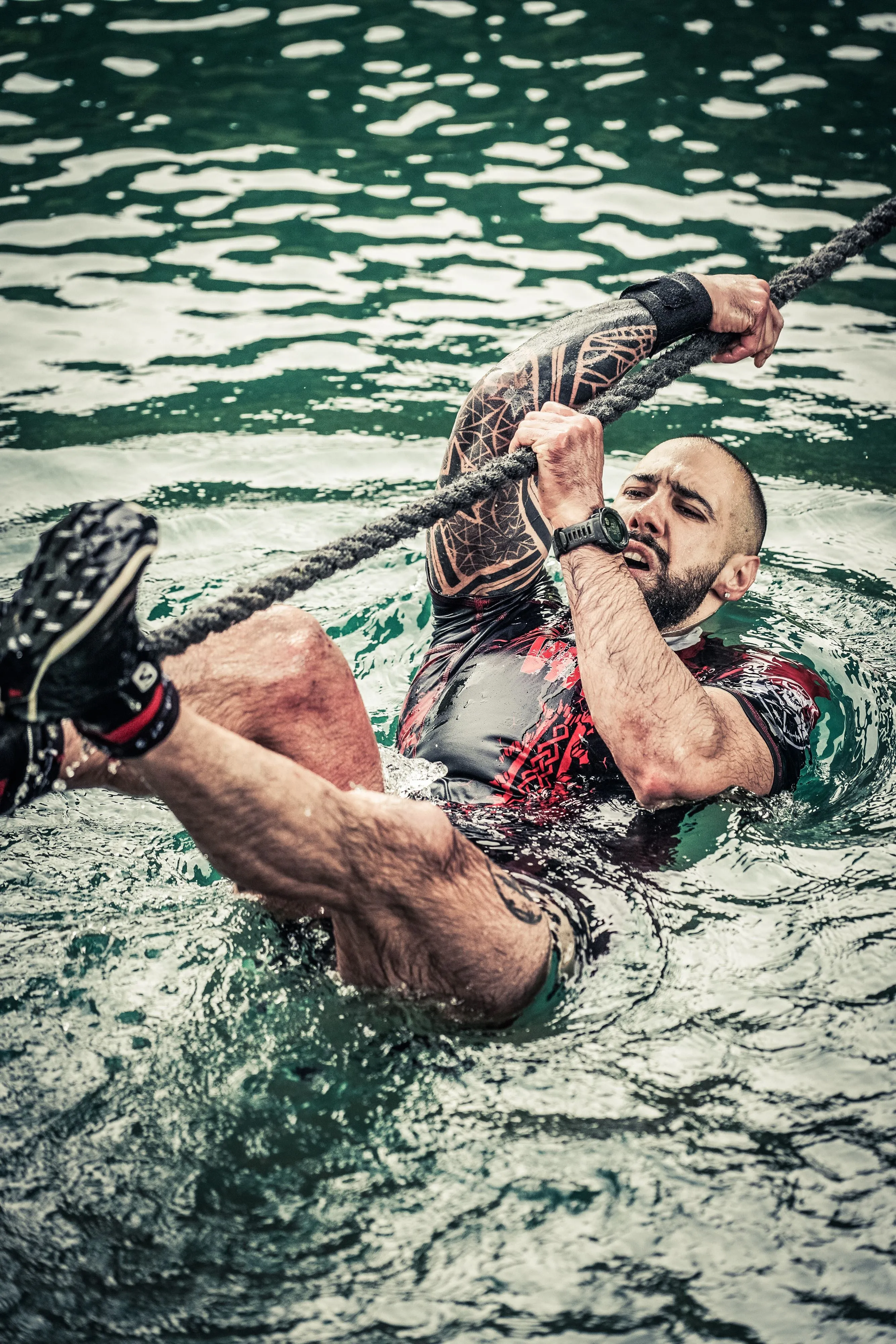 OCR athlete pulling himself along a rope through the water at the X-Warriors obstacle race in Molveno