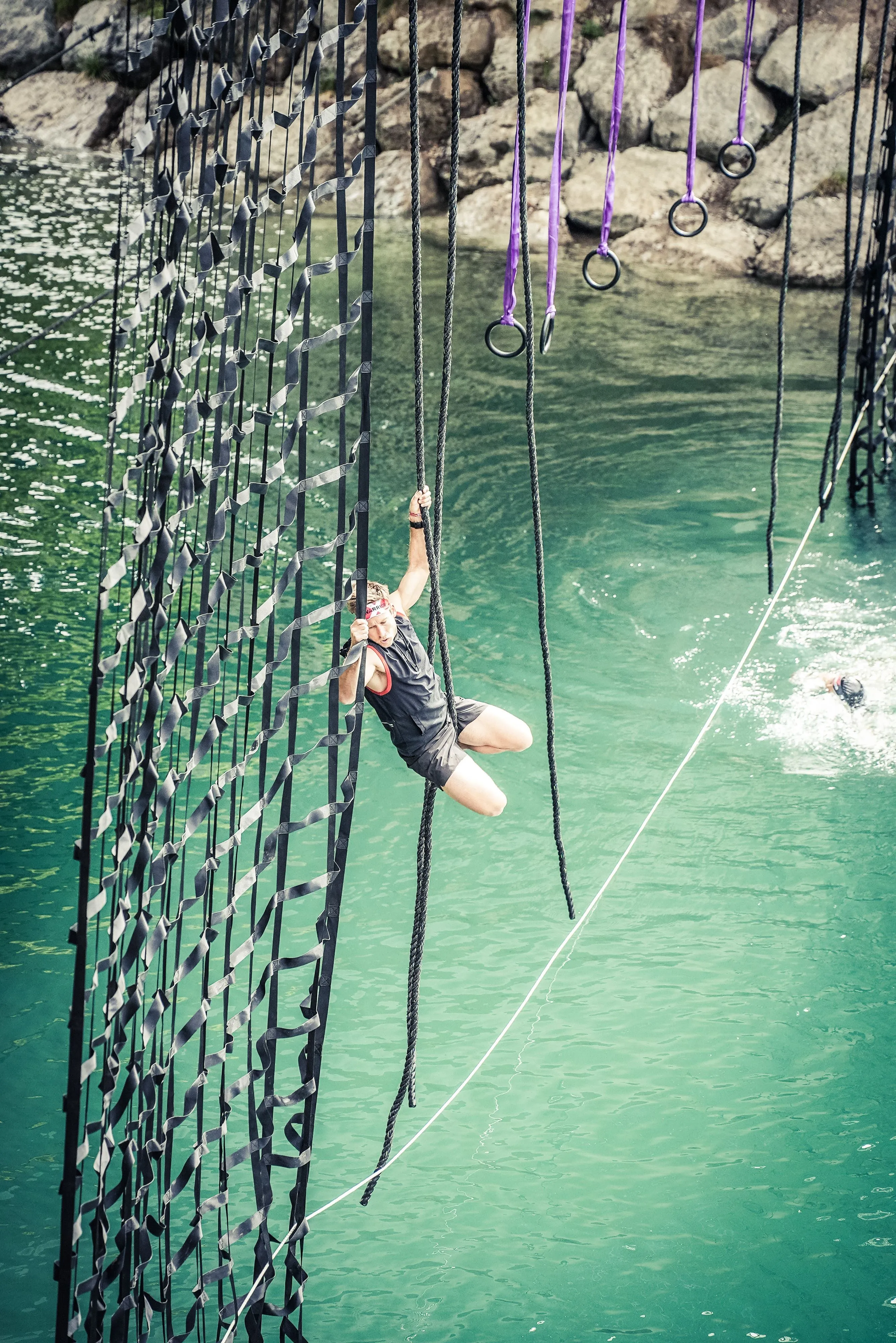 X-Warriors athlete hanging from ropes and nets over Lake Molveno during the obstacle race