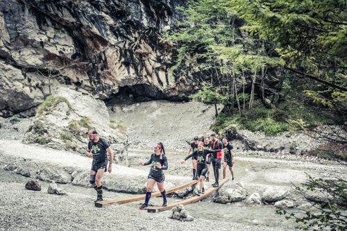 Group of friends balancing together over a small water current, smiling and having fun during the X Warriors race.