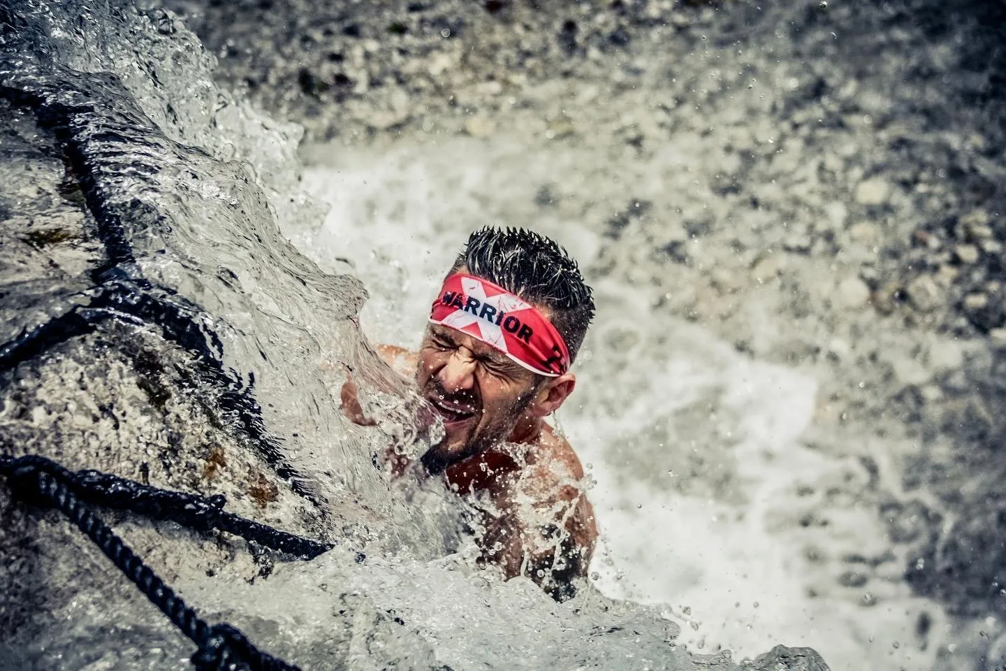 Athlete pushing through a waterfall on a rope at the X-Warriors OCR race in Molveno