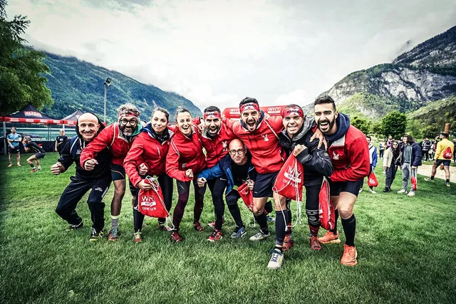 X-Warriors team in red jackets celebrating in the Molveno race village with the Dolomites behind
