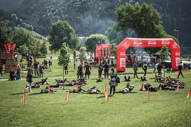 Athletes stretching on the lawn in front of the Why Sport arches at the X-Warriors race village in Molveno