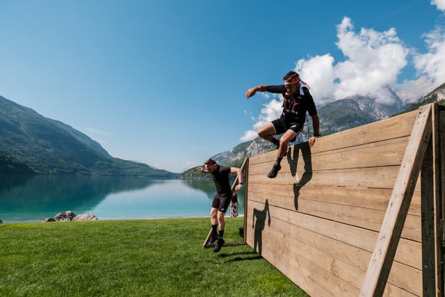 Two men climbing a log in the water with many rocks and stones in the background during the X Warriors race.