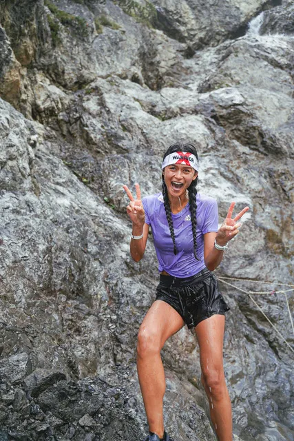 Female athlete making peace signs in front of a rock wall at the X-Warriors obstacle race in Molveno
