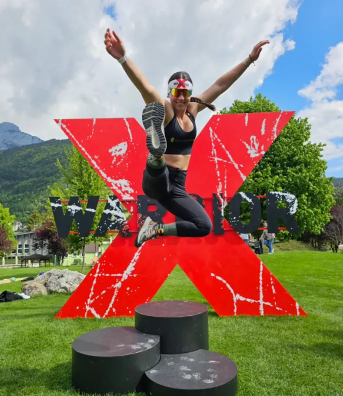 Female athlete jumping in celebration in front of the giant red X-Warriors X in Molveno