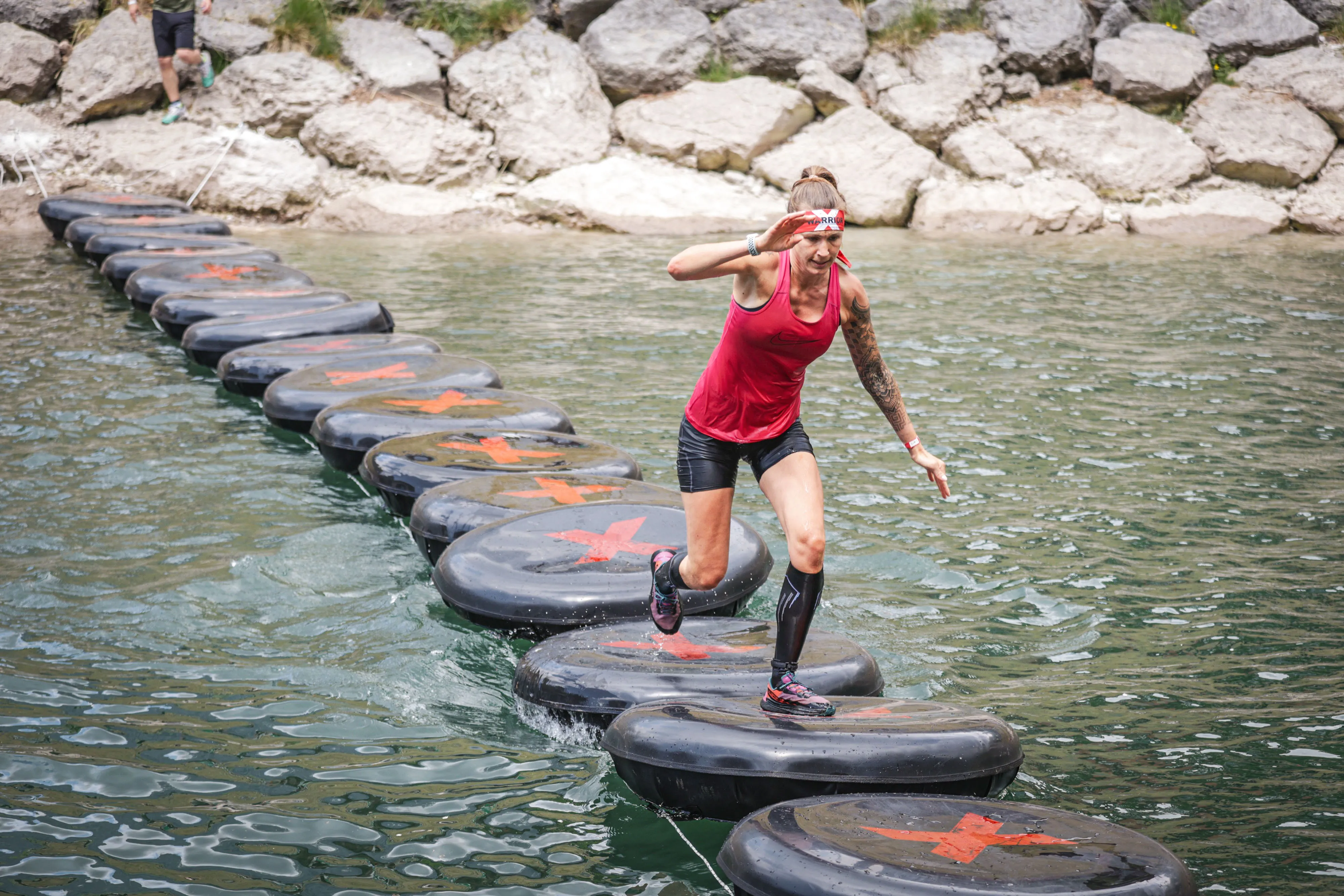 Female athlete running across floating tyres on the lake at the X-Warriors obstacle race in Molveno