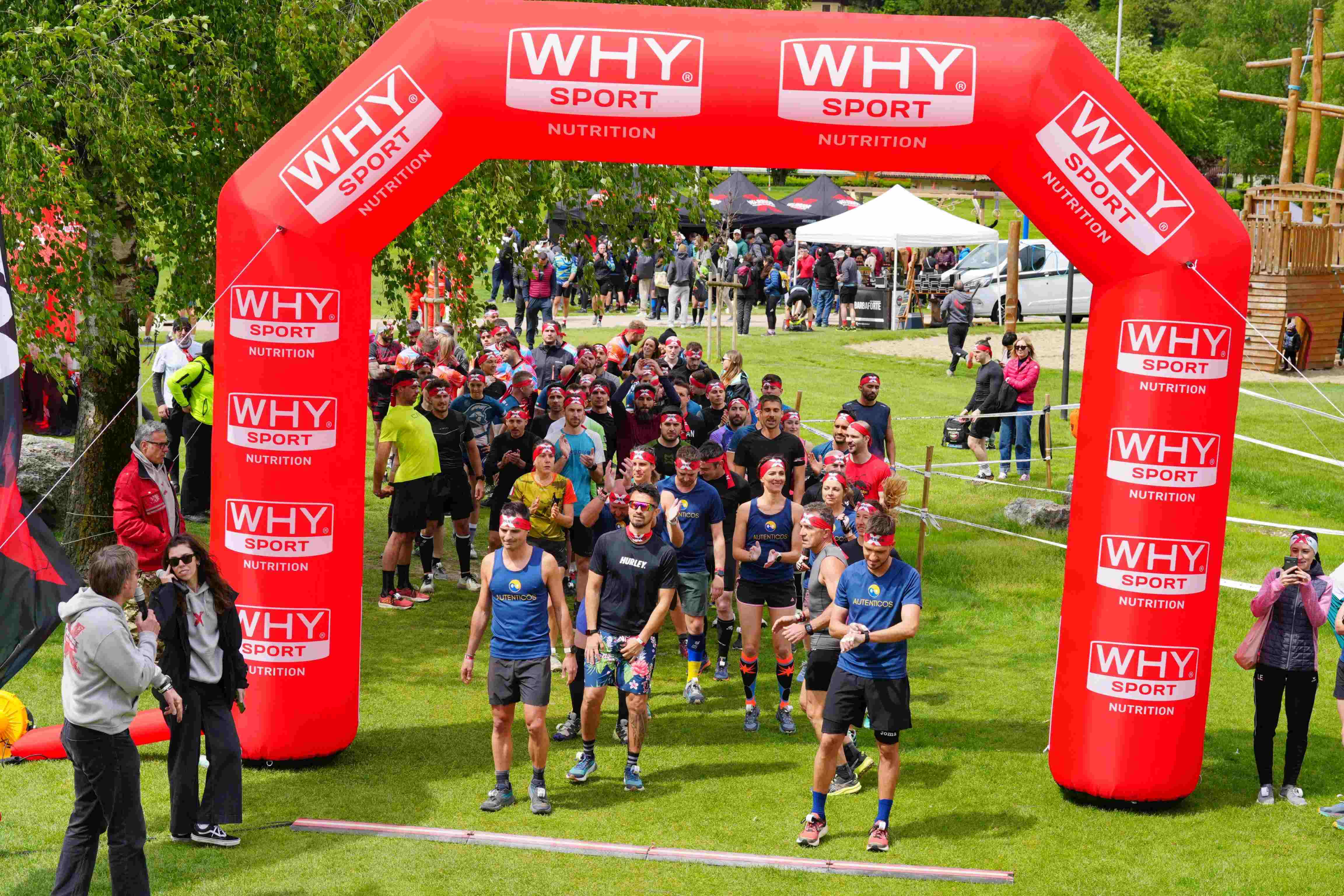 Three OCR athletes on the starting line of the X Warriors event under a Why Sport sponsor arch, with green Dolomites nature in the background.