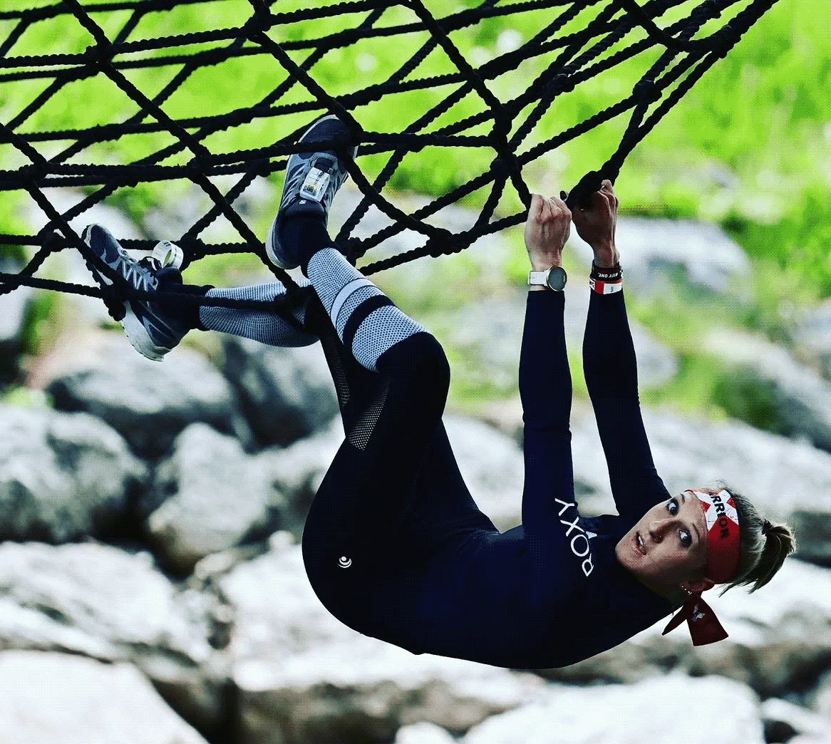 Female athlete hanging upside down from a cargo net at the X-Warriors obstacle race in Molveno