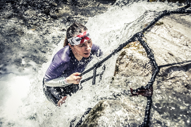 Female athlete climbing a net through a rushing waterfall at X-Warriors Molveno