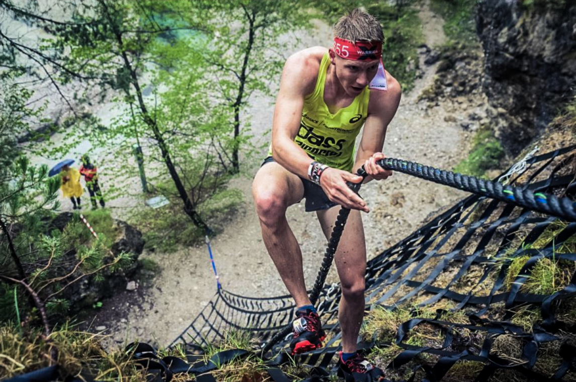Charles Franzke climbing a rope net in the forest during an obstacle race