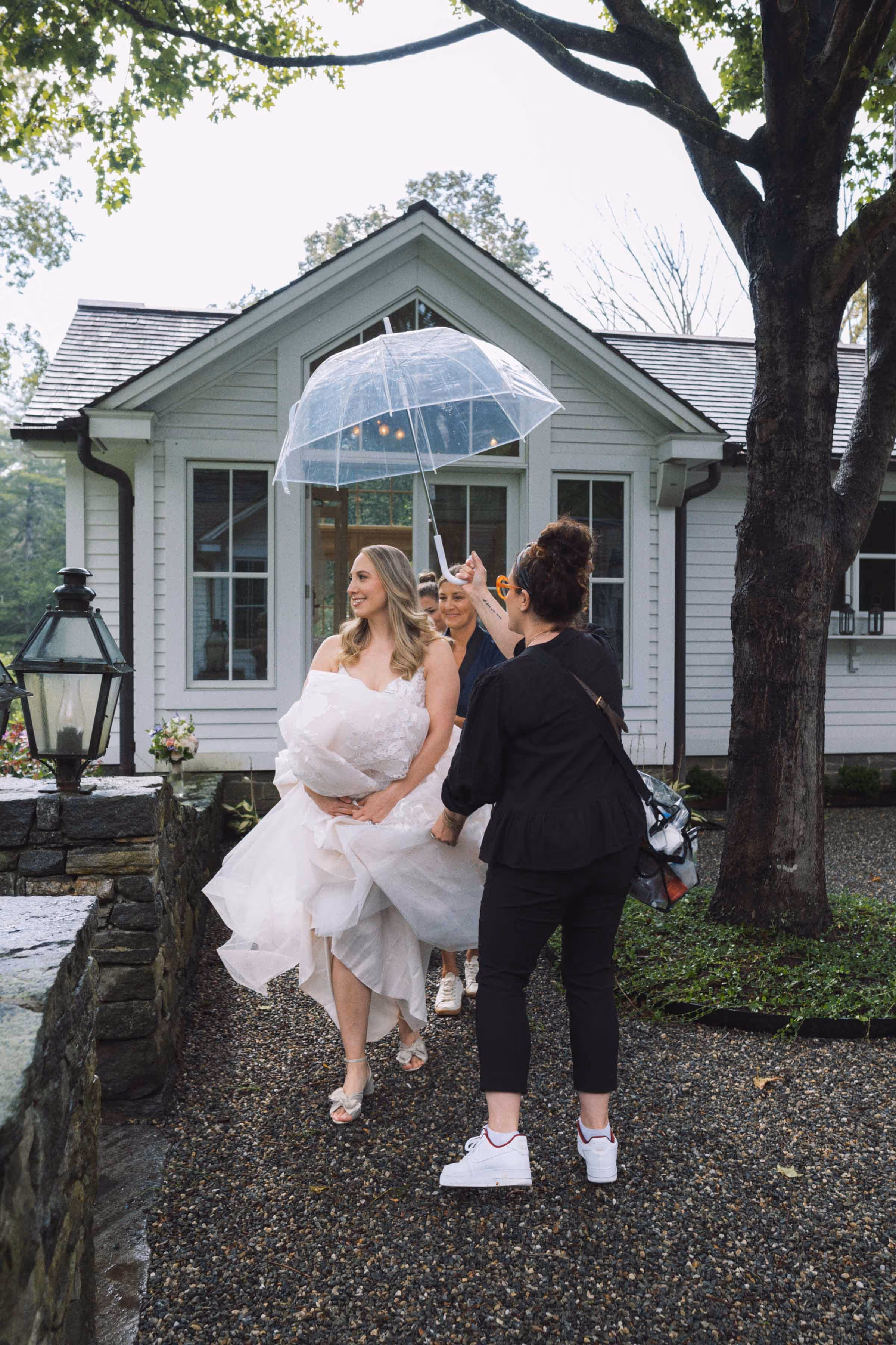 Bride steps outside for the couple's first look on a rainy day as the wedding planner holds an umbrella over her