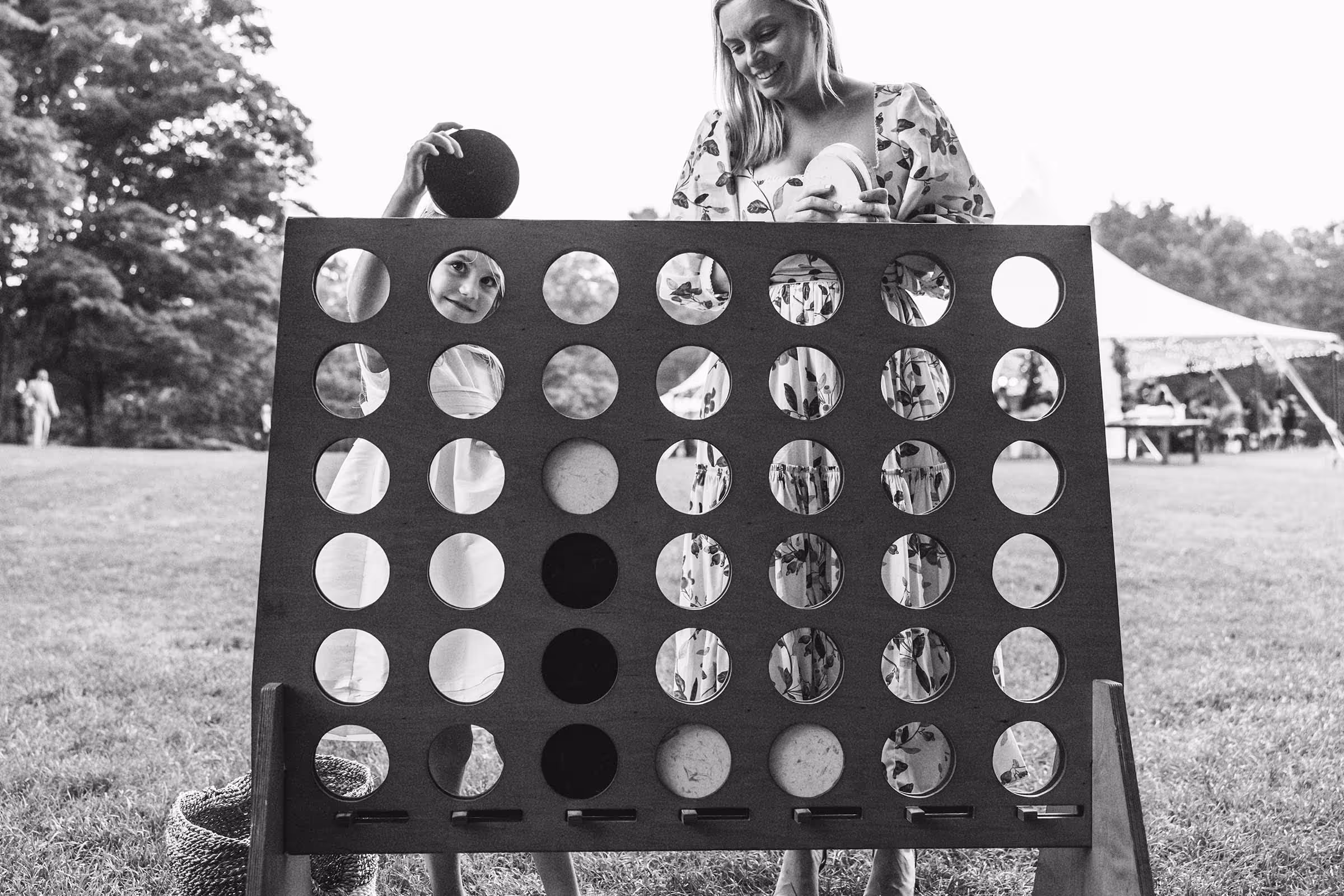 Black and white image of a youn girl and her mother playing a large yard version of connect four at wedding reception