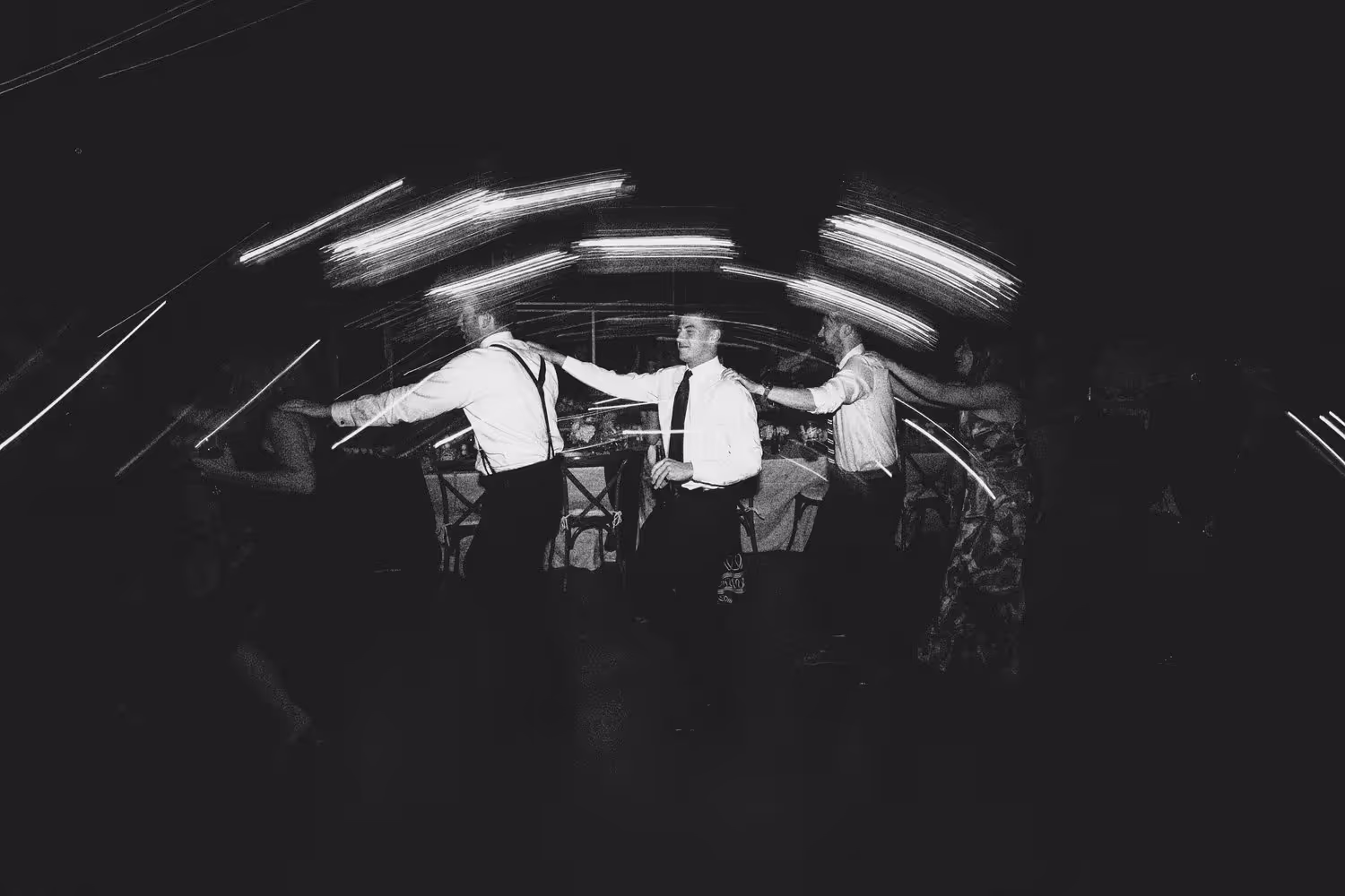 Black and white image of wedding guests dancing in a conga line