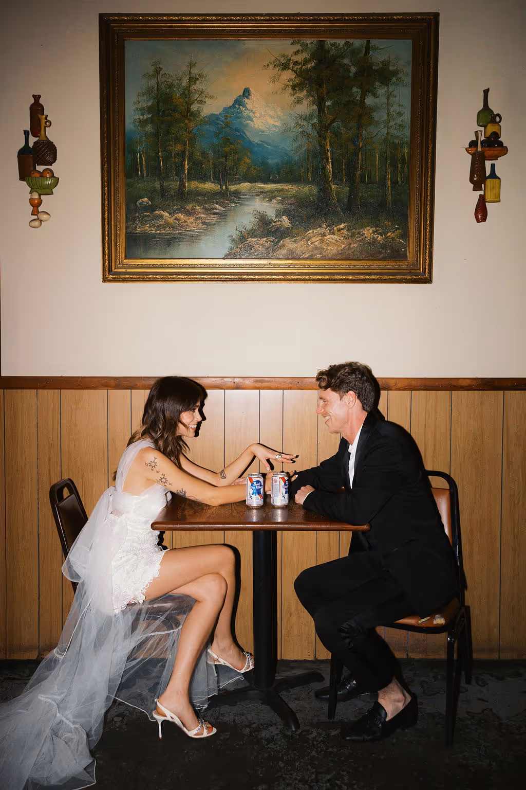 Engaged couple sit across from each other in a white dress and suit as they recreate their first date night in documentary style engagement session at Welcome To The Johnsons in NYC