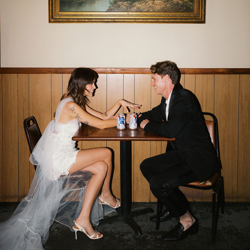 Engaged couple sit across from each other in a white dress and suit as they recreate their first date night in documentary style engagement session at Welcome To The Johnsons in NYC