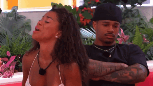 A woman in a white bikini appears emotional and is yelling or crying, while a man in a black shirt and hat sits behind her with his arms crossed, looking away uninterested.