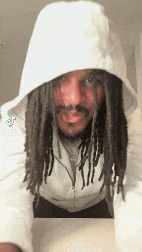 A person with long dreadlocks, wearing a white hoodie, leans forward dancing and smiles at the camera