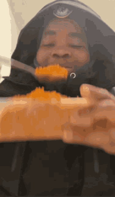 A man wearing a black jacket with a hood and eating jollof rice from a plastic bowl.