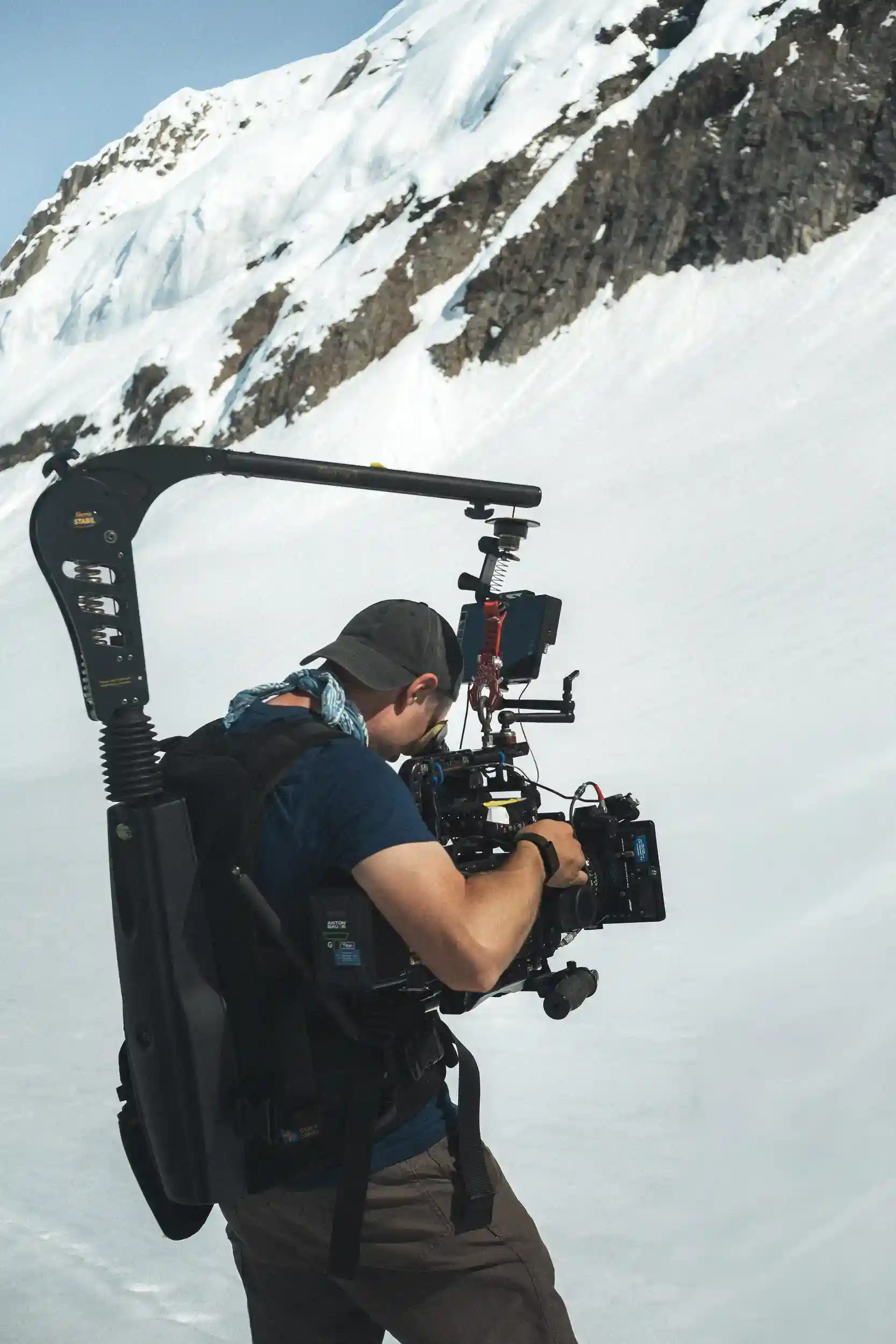 Camera operator shoots with ARRI camera on Easyrig stabilizer below a mountain ridge in Alaska