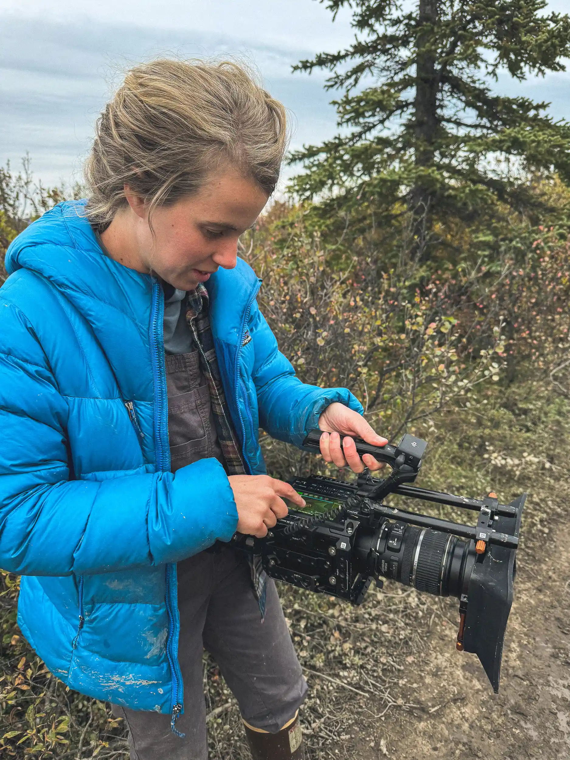 `Camera operator adjusts settings on a Blackmagic cinema camera on a tundra trail in Alaska`